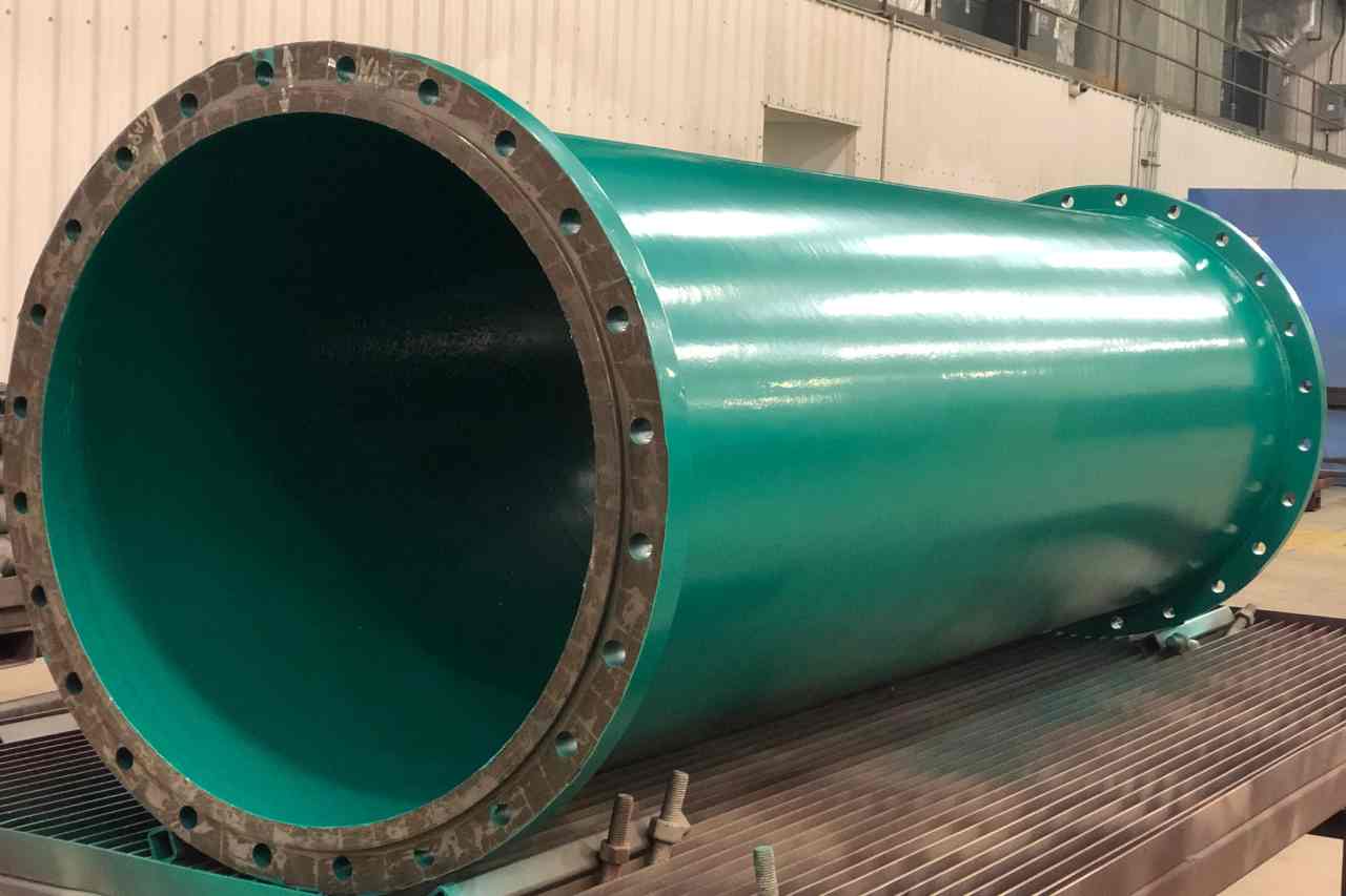 A large pipe in a green protective coating sits in a warehouse.