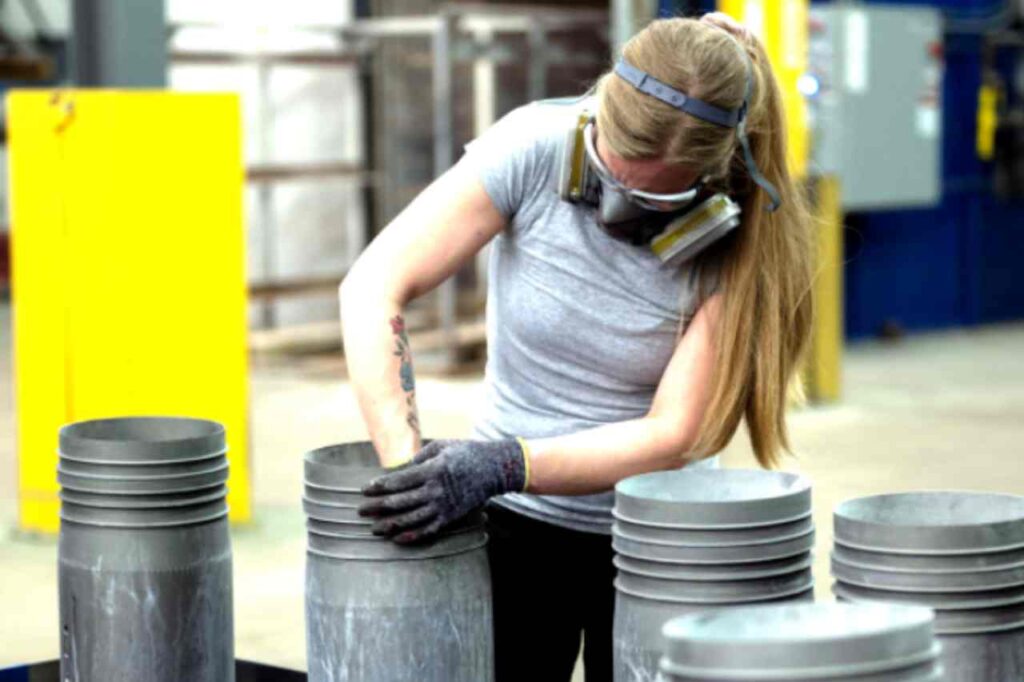 A woman in a respirator mask working on coating metal materials in a warehouse.