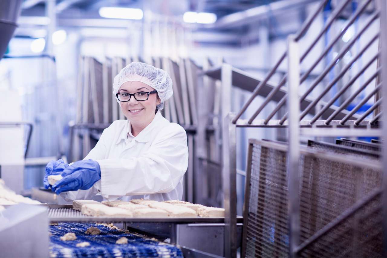 A female worker wearing a hair net works in a food manufacturing plant.