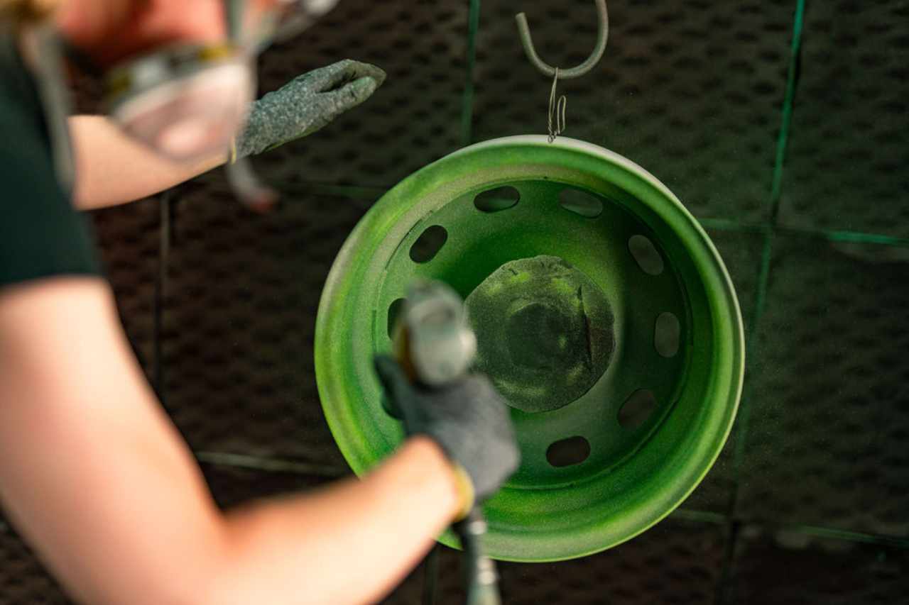 A technician applies green powder coating through a spray gun in the IPC shop.