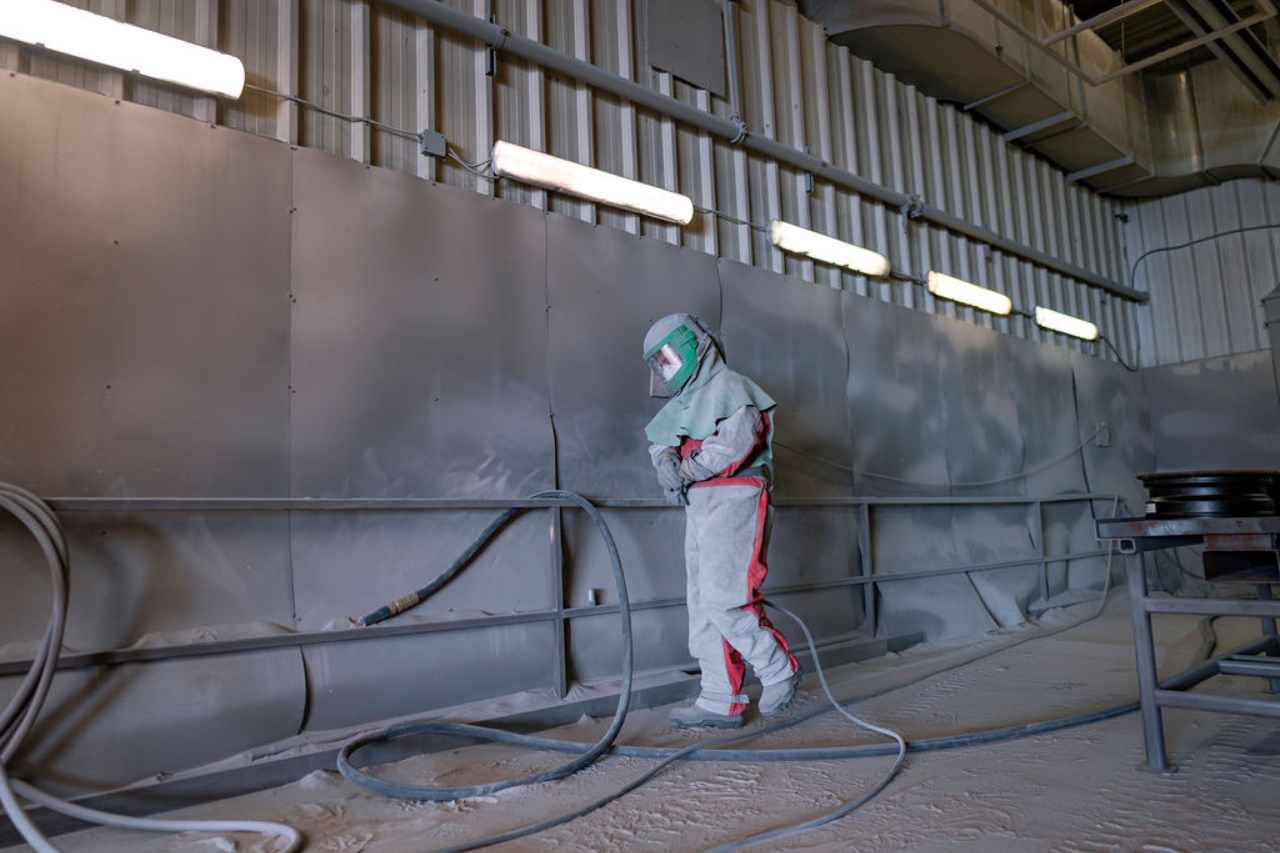 A technician in PPE in our sandblasting room, as we begin to process equipment for the powder coating process.